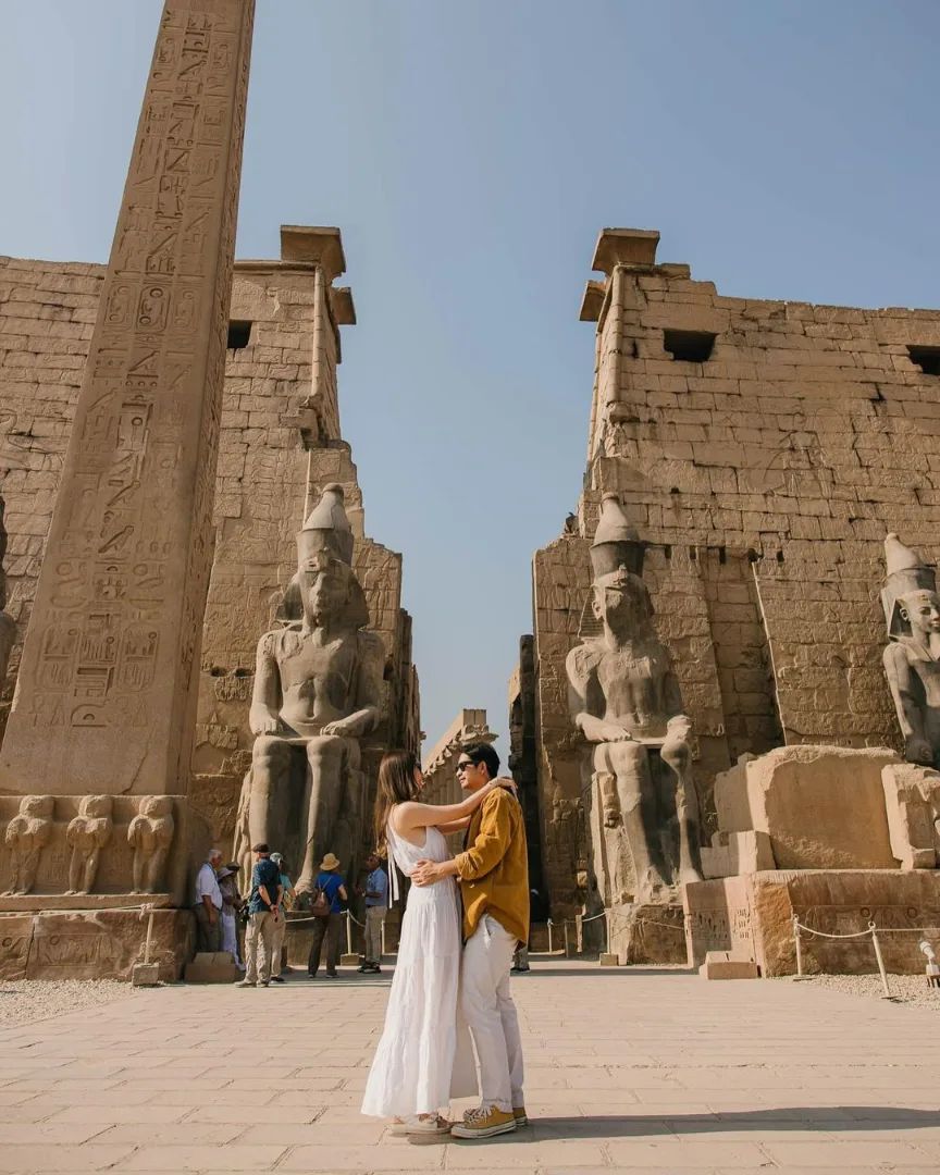 Couple at the entrance of Luxor Temple with obelisk and colossi of Ramses, Egypt